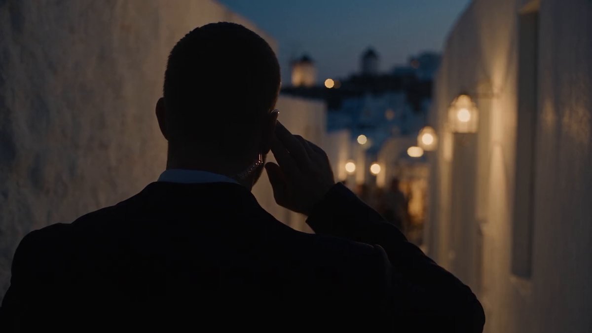 Close protection officer on comms in a Mykonos lane at dusk