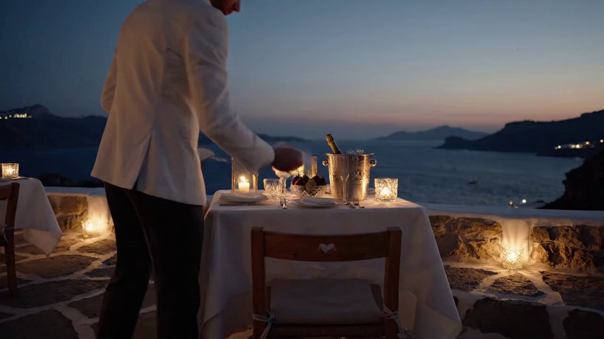 A reserved table laid for two on a stone terrace above the sea at dusk in Mykonos