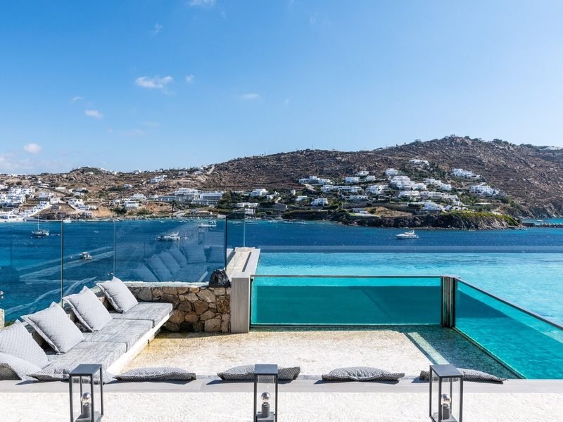 Infinity pool with glass edge overlooking a turquoise bay and whitewashed hillside, Mykonos