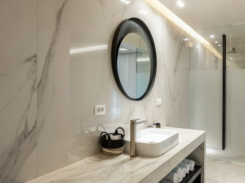 Marble bathroom vanity with vessel basin, round black mirror and walk-in glass shower
