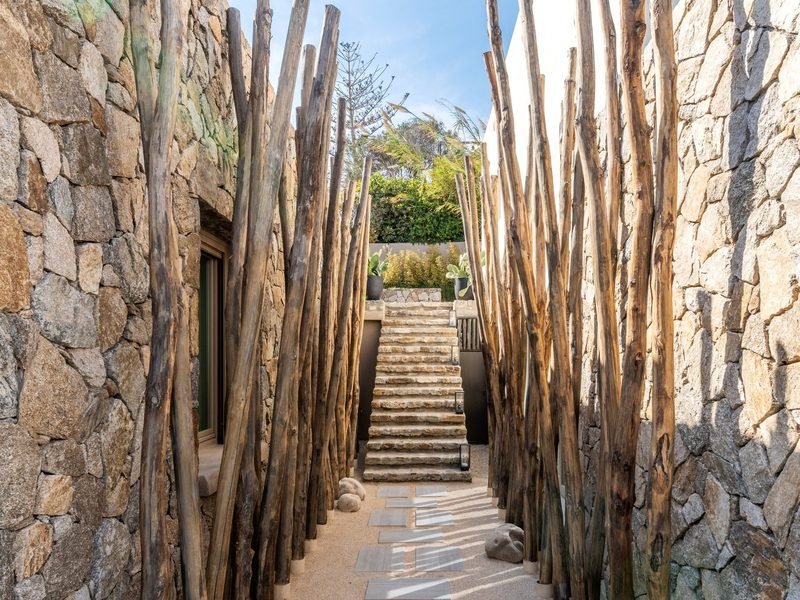Stone passage lined with driftwood poles leading up a flight of stepped slabs