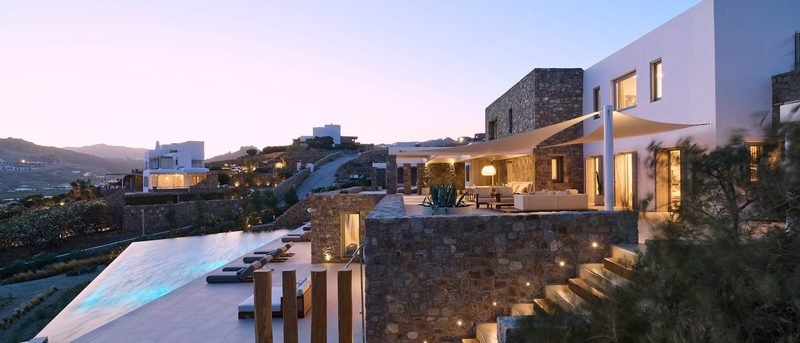 The estate at dusk with its lit pool terrace, shaded lounge and stone wings, Kalafatis