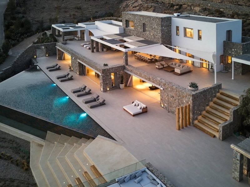 Pool terrace seen from above at dusk, pergola dining area beside stone-clad wings