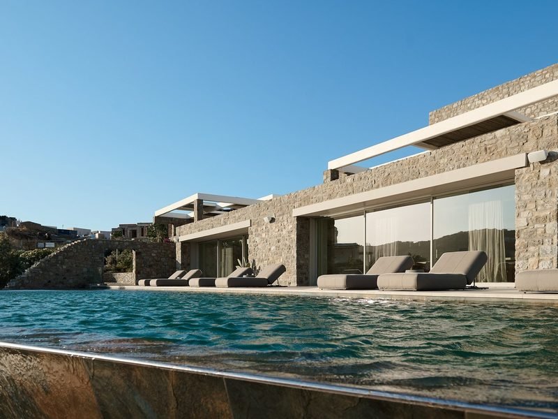 Infinity pool seen from the waterline, loungers set along the stone and glass frontage