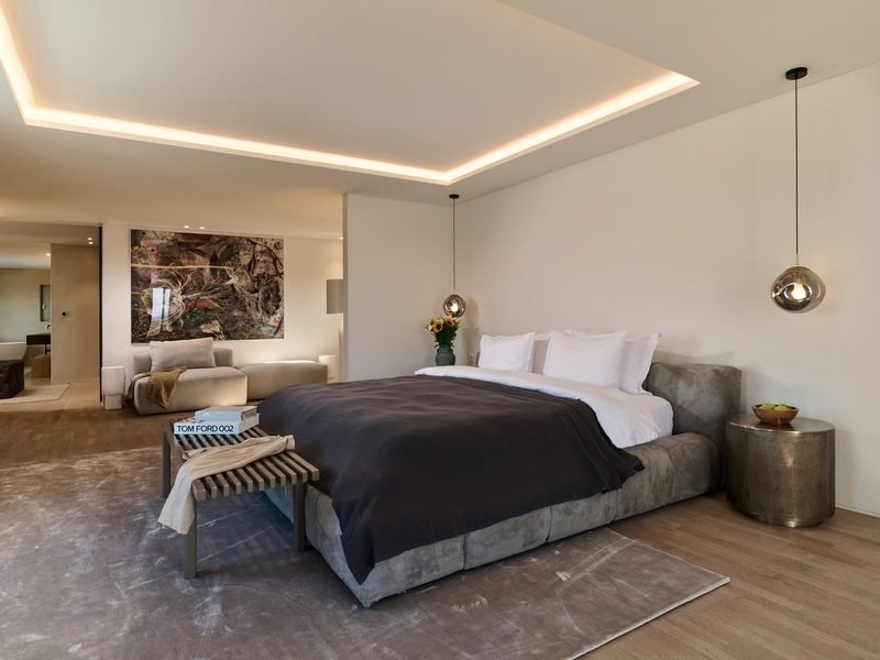 Bedroom suite with cove-lit ceiling, brass pendants and a lounge seating area beyond
