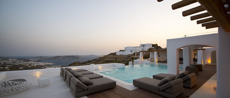 Infinity pool and day beds on a lit terrace at dusk, the Agia Sofia hillside