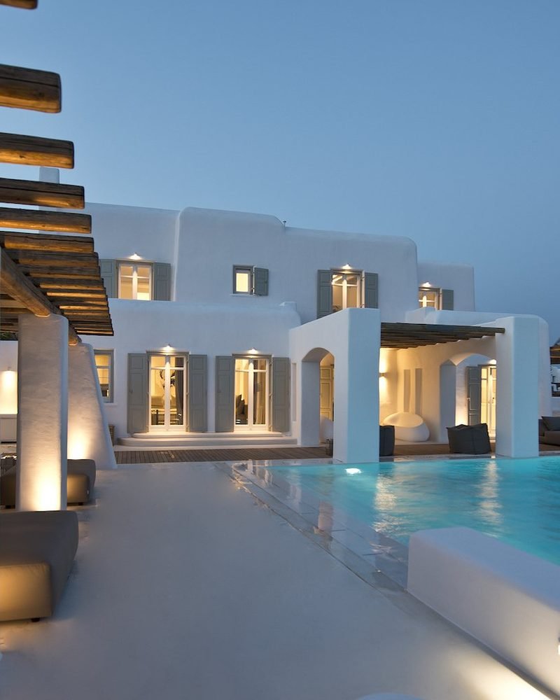 Lit villa facade and pergola reflected in the pool at blue hour