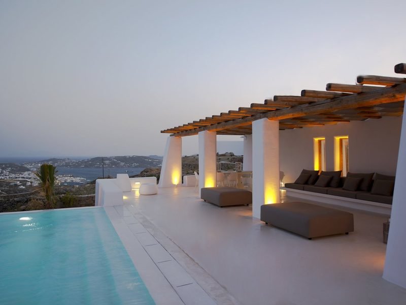 Pergola lounge with backlit niches and low sofas beside the infinity pool at dusk