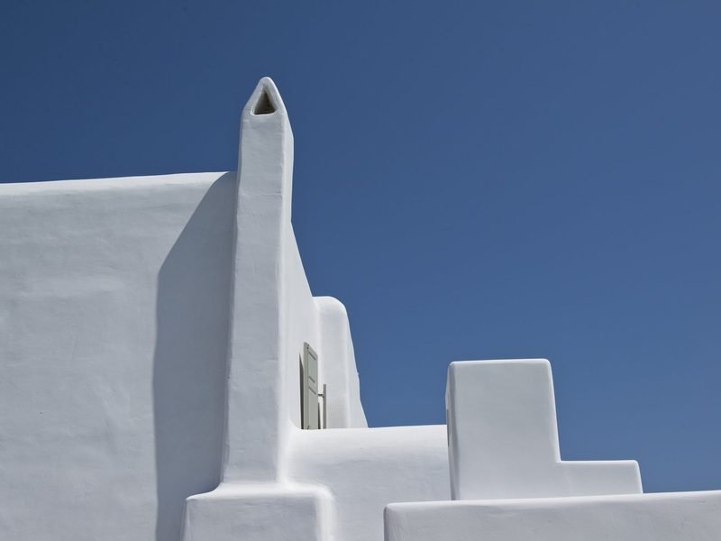 Whitewashed roofline, chimney and stepped parapet against deep blue sky