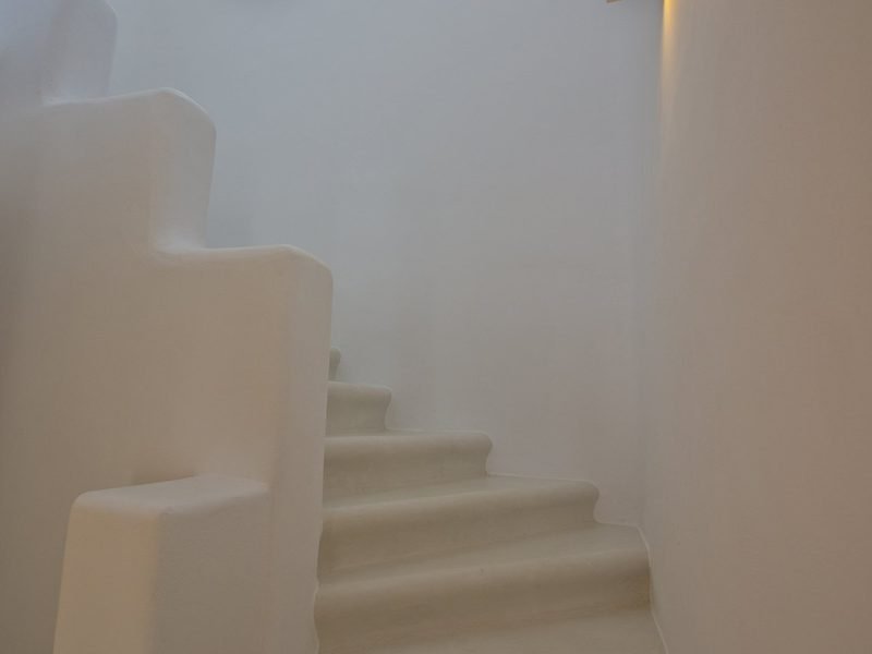 Sculpted plaster staircase curving upward between whitewashed walls, warm light from above