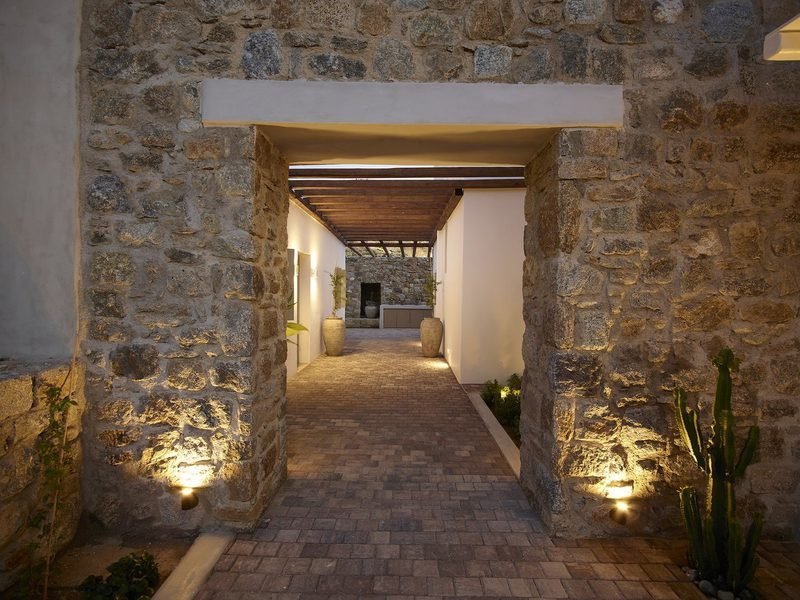 Stone-walled entrance passage lit at night, potted plants and timber pergola ahead