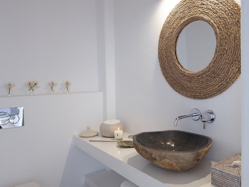 Bathroom vanity with a carved stone basin, round woven mirror and lit candle