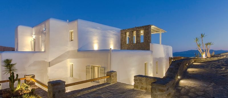Whitewashed villa lit at blue hour above lantern-lit stone terraces and steps, Elia