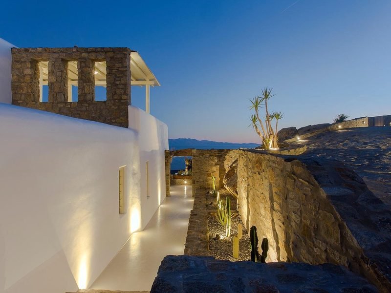 Whitewashed walkway between stone terraces and cacti, sea and mountains beyond at dusk, Elia