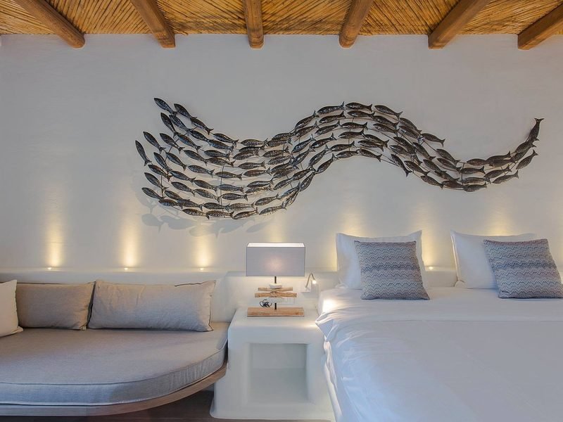 Bedroom with a metal shoal-of-fish wall sculpture above white linen and a built-in daybed