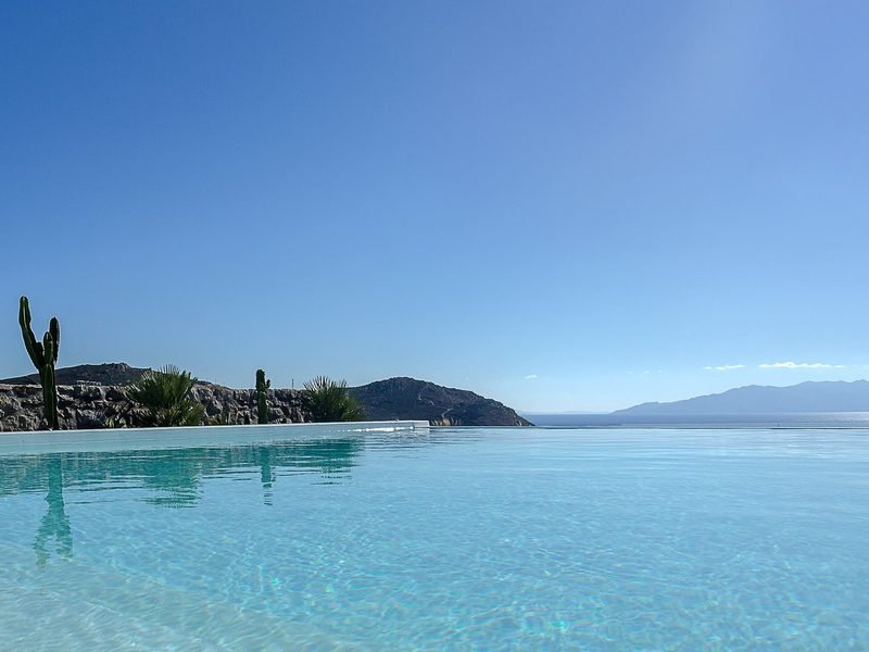 Water-level view across the infinity pool to headland, open sea and clear sky, Elia