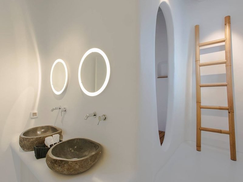 Twin river-stone basins on a white plaster ledge below two backlit oval mirrors