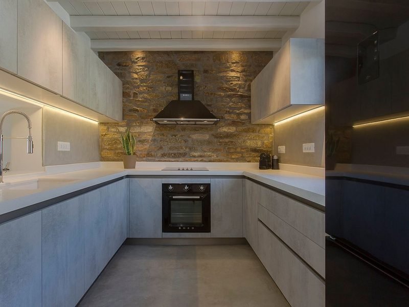 U-shaped kitchen with grey cabinetry, white worktops, exposed stone wall and black extractor hood