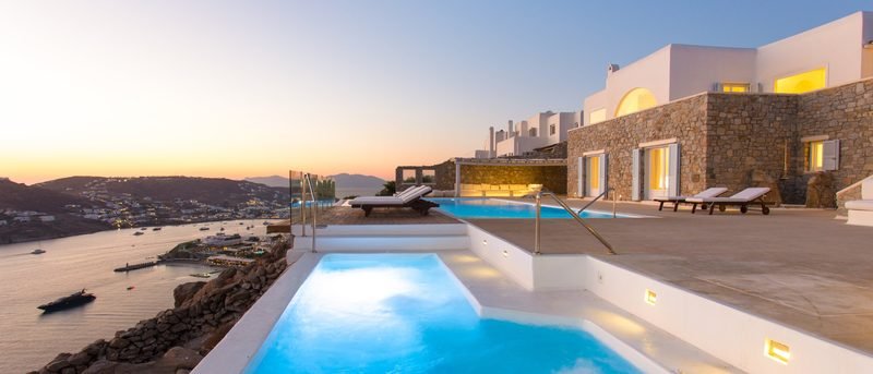 Twin lit pools and terrace above a yacht-filled bay at sunset, Agios Lazaros / Ornos