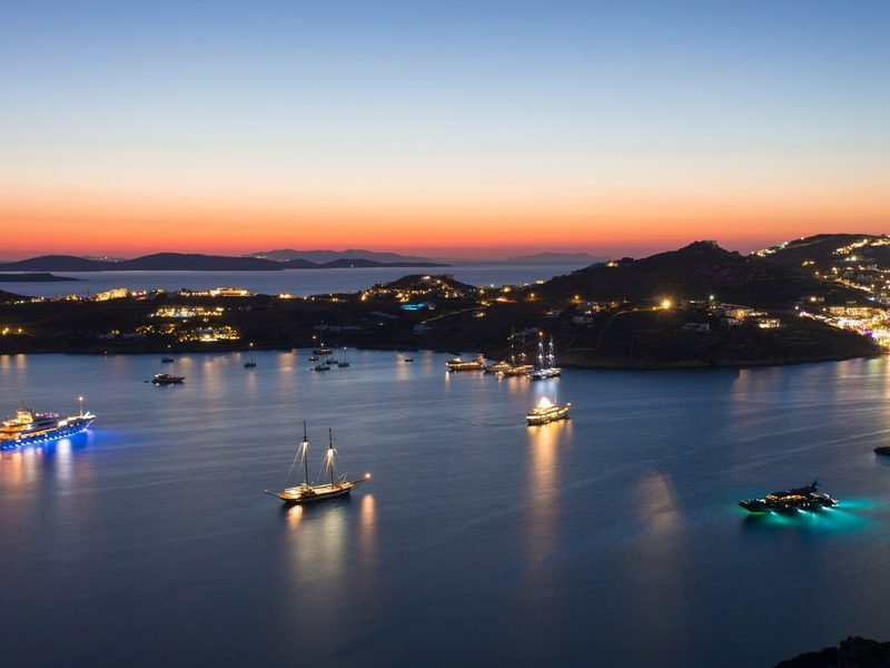 The bay seen from above at dusk, yachts lit on dark water, Agios Lazaros / Ornos