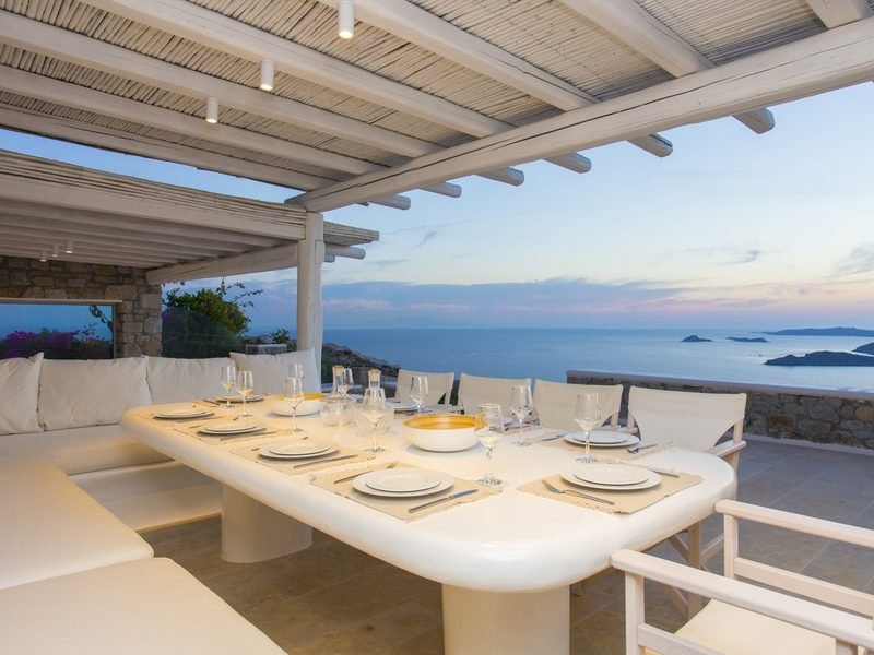 Pergola dining table set with white china under reed beams, sea beyond, Agios Lazaros / Ornos