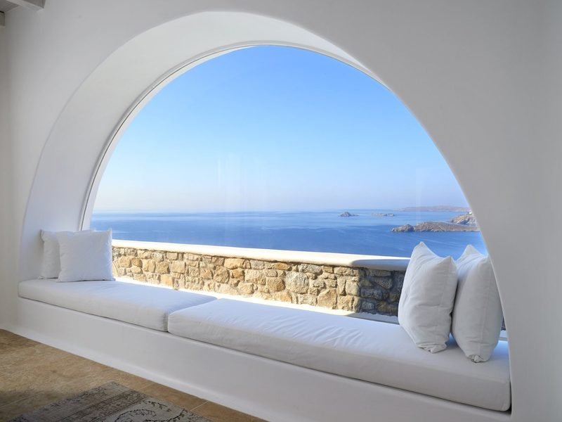 Arched window seat with white cushions framing the sea and a rocky islet