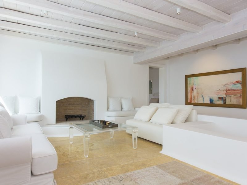 Open-plan living room with white built-in sofas, sculpted fireplace and framed abstract painting