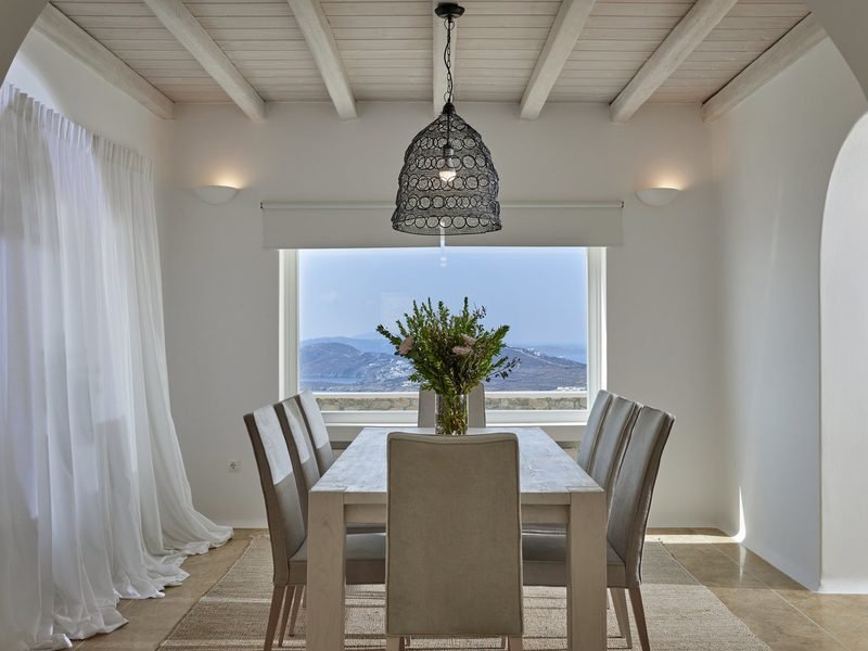 Indoor dining table beneath a woven pendant lamp, picture window over the hillside