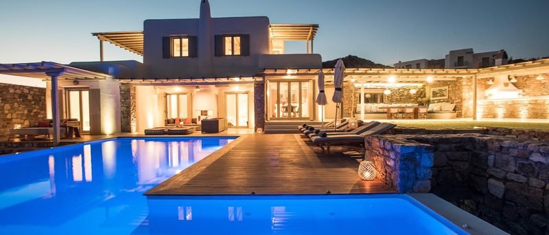Villa lit at dusk above a glowing pool and teak deck, Kalafatis / Ano Mera