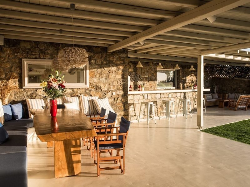 Covered terrace dining table in live-edge wood beside a stone bar with metal stools