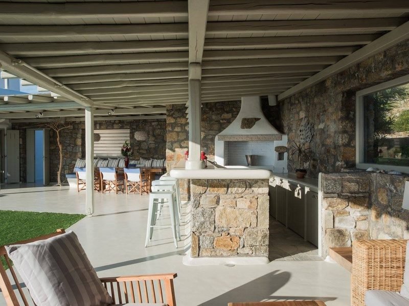 Outdoor kitchen island in stone with breakfast stools under a beamed pergola