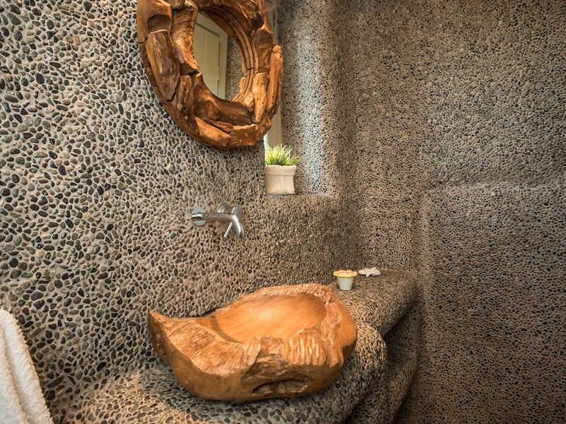 Pebble-mosaic shower room with a carved teak basin and round driftwood mirror