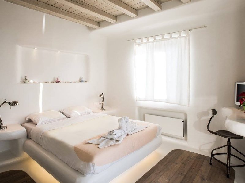 Bedroom with low platform bed, lit plaster niche and exposed timber ceiling beams