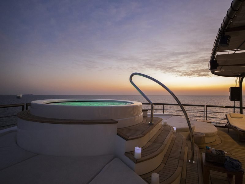 Deck spa pool lit at dusk, teak steps and candles facing an open horizon