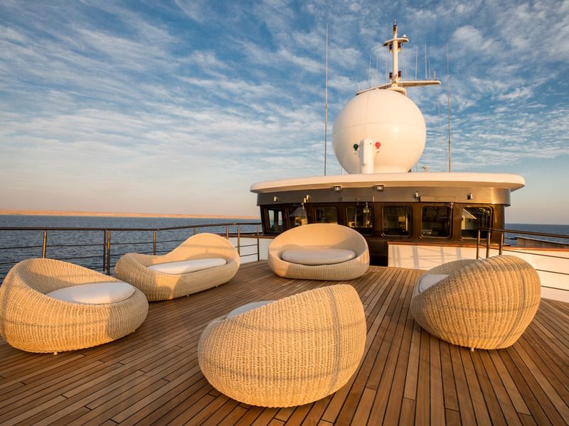 Sun deck at golden hour, wicker lounge pods on teak below the wheelhouse radome