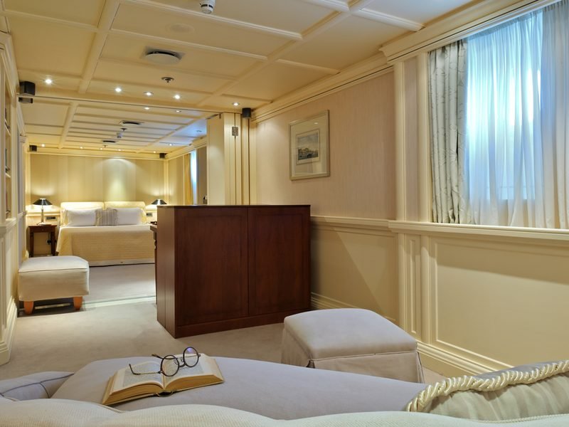 Guest suite in cream panelling, sitting area foreground and bed beyond a mahogany divider