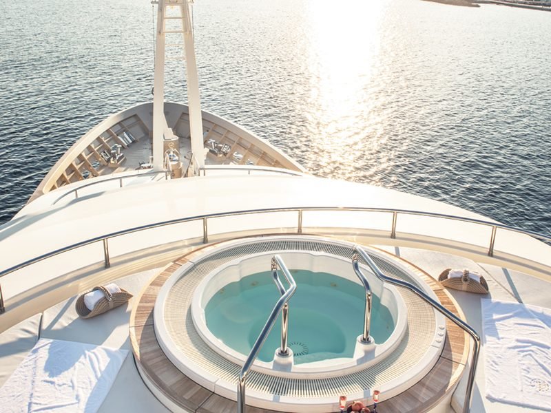 Deck jacuzzi and sunpads at sunset, looking forward over the bow to an anchorage