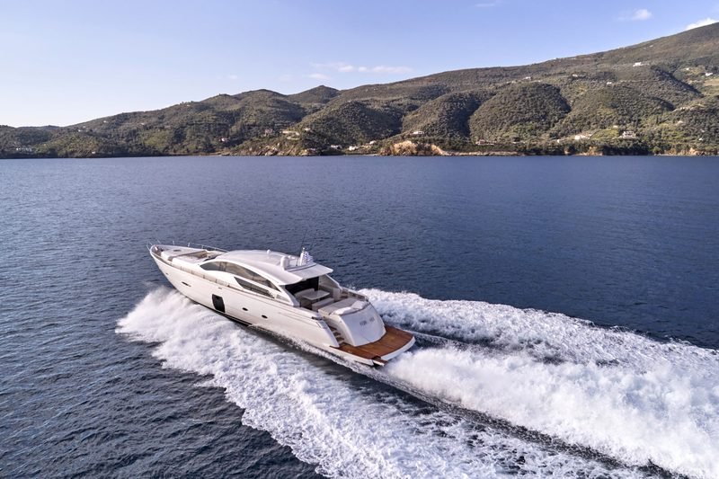Motor yacht FOR EVER underway at speed, wake fanning out below a green Greek coastline