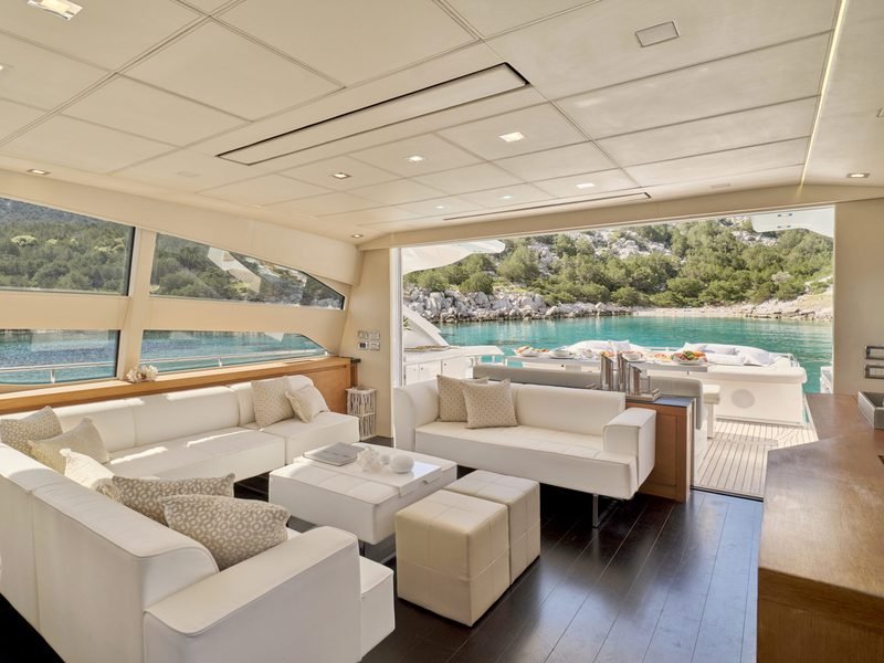 Main saloon with white lounge seating opening through full-width glass to the aft deck