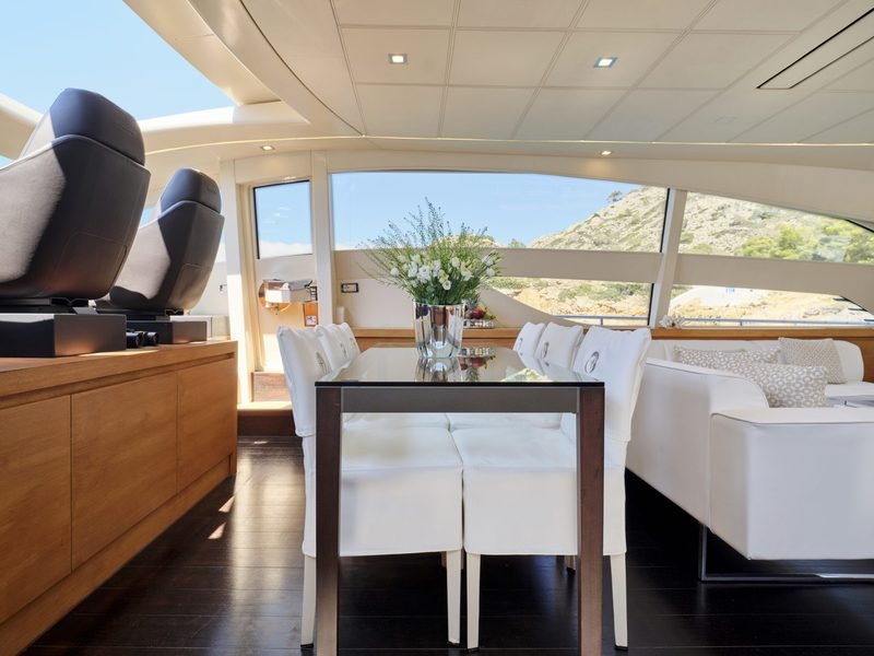 Indoor dining table in glass and dark wood, white flowers and helm seats behind