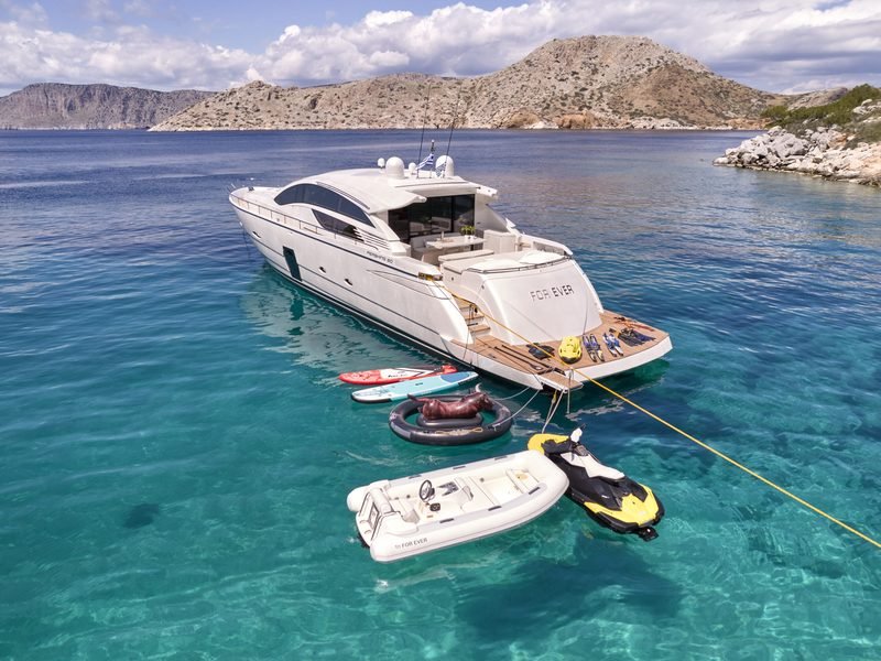 Aerial at anchor in a rocky cove with tender, jet ski and paddleboards astern