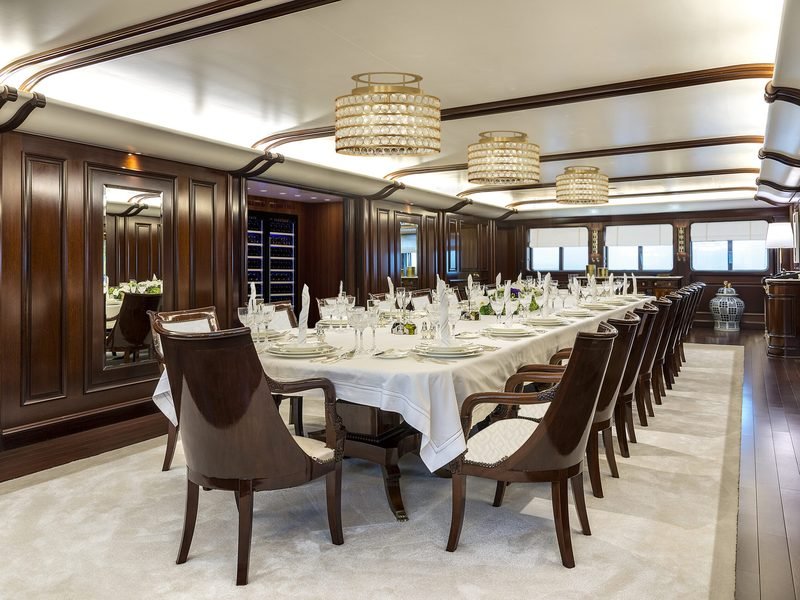 Formal dining saloon with a long laid table, mahogany panelling and lit wine wall
