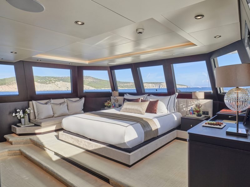 Master cabin with full-beam bed on a raised platform and panoramic coastal windows