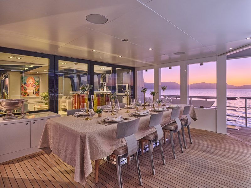 Aft deck dining table dressed at dusk, violet sunset over distant mountains