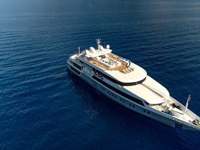Aerial of the yacht at anchor on deep blue water, sun deck pool visible