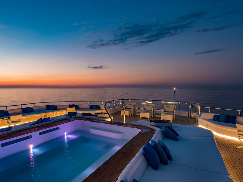 Sun-deck pool lit lavender at blue hour, teak decking and navy cushioned seating