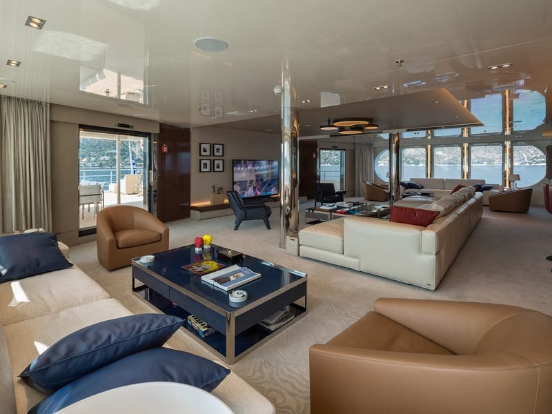 Main saloon with oval panoramic windows, leather sofas, bar stools and coastline beyond