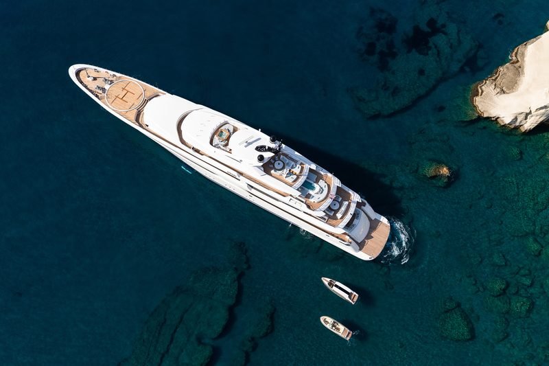 Aerial of the white motor yacht at anchor over turquoise water, tenders alongside
