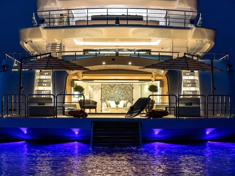 Illuminated beach club open to the sea at night, underwater lights glowing violet