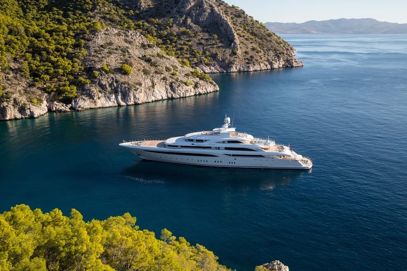 Motor yacht at anchor in a pine-fringed Greek cove, deep blue water